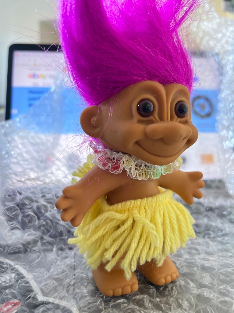 troll figurine Hawaiian doll with magenta pink hair, lace flower ribbon around neck, yellow wool thread skirt representing a straw skirt 